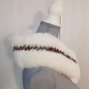 May include: White faux fur collar with a brown and pink braided trim. The collar is displayed on a gray mannequin.