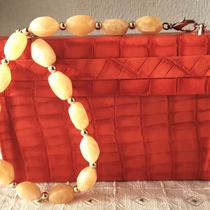 May include: A bright orange crocodile-embossed clutch bag with a gold chain and a yellow beaded strap.