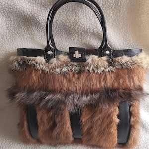 May include: A brown and black fur tote bag with leather handles and trim. The bag has a unique design with alternating strips of fur and leather.