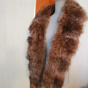 May include: A brown fur collar with a long, fluffy texture. The collar is displayed on a white mannequin.