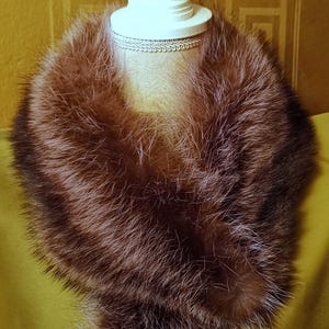May include: A brown fur collar on a white mannequin. The collar is thick and fluffy, and it is wrapped around the mannequin's neck.