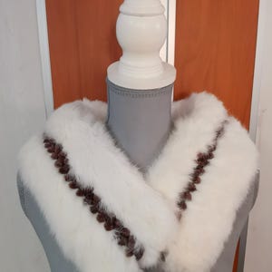 May include: White faux fur collar with brown trim. The collar is displayed on a mannequin.
