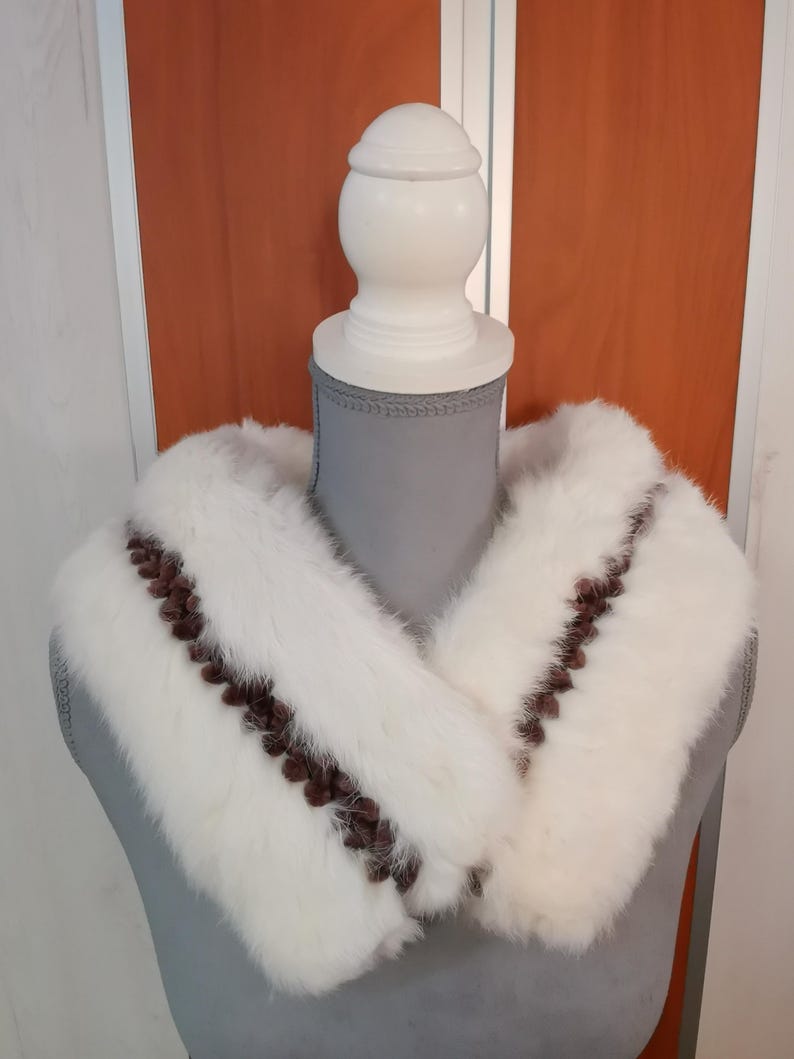 May include: White faux fur collar with brown trim. The collar is displayed on a mannequin.