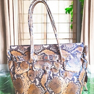 May include: A brown and black snakeskin tote bag with a silver buckle and a top handle.