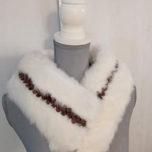 May include: White fur collar with brown trim. The collar is displayed on a white mannequin.