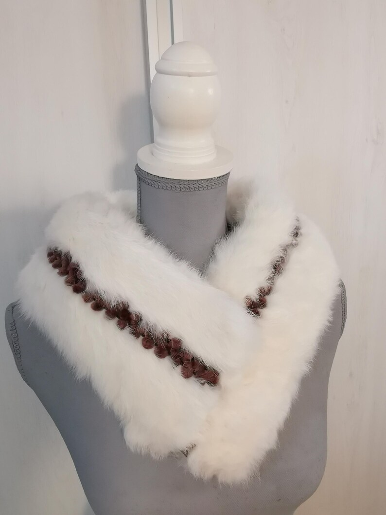 May include: White fur collar with brown trim. The collar is displayed on a white mannequin.