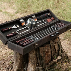 May include: A wooden carrying case containing a set of metal skewers and a small metal bowl. The case is open and the skewers are arranged neatly inside.