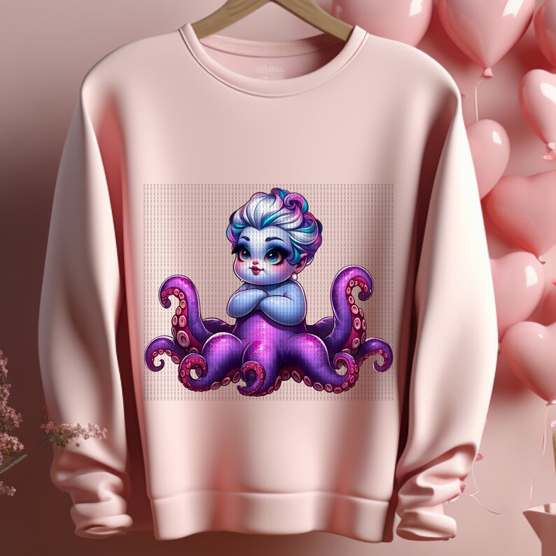 Pu&ograve; includere: Una felpa rosa con un'illustrazione di un polpo viola con un personaggio femminile blu e bianco seduto sopra. Il personaggio indossa una corona e un vestito viola.