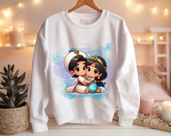 May include: White sweatshirt with a cartoon image of Aladdin and Jasmine from Disney's Aladdin. The characters are depicted in a romantic embrace, with Aladdin holding Jasmine in his arms. The image is set against a blue and purple watercolor background with sparkling stars.