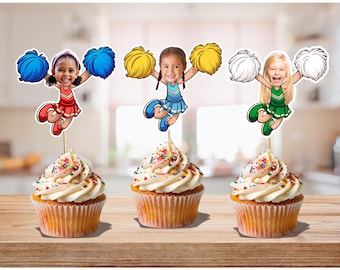 May include: Three cupcakes with white icing and colourful sprinkles. Each cupcake is topped with a cheerleader figure holding pom-poms. The cheerleaders wear red, blue, and green outfits, and have different skin tones and hair colours.
