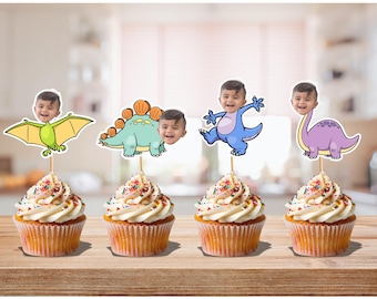 May include: Four cupcakes with white frosting and colorful sprinkles. Each cupcake is topped with a dinosaur-themed cutout featuring a child's face. The dinosaurs are green, blue, purple, and yellow.