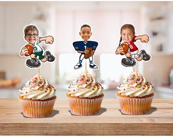 May include: Three cupcakes with white icing and colourful sprinkles. Each cupcake is topped with a cartoon image of a child in a football uniform holding a football. The cupcakes sit on a wooden surface.