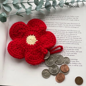 May include: A red crocheted flower with a yellow center, resting on a book with the text "Come Look With Me Exploring Landscape Art with Children."  The flower is holding a pile of US coins.