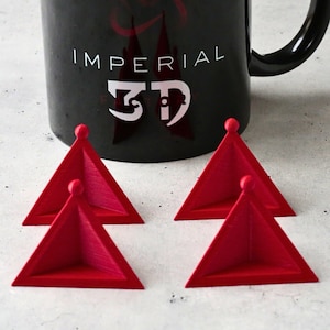 Può includere: Quattro pezzi da gioco triangolari rossi si trovano davanti a una tazza nera con le parole "Imperial 3D" stampate su di essa.