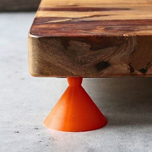 May include: A wooden cutting board with a natural wood finish and orange rubber feet. The board is made of multiple pieces of wood, creating a unique pattern.