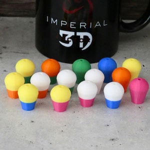 May include: A collection of 14 colorful, two-toned, 3D printed gaming dice with a white, yellow, blue, green, pink, orange, and red color scheme.