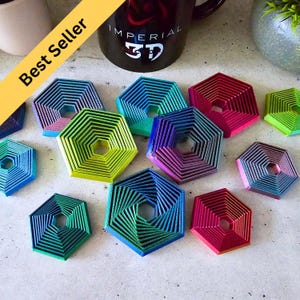 May include: A set of 10 colourful, multi-layered, hexagonal coasters with a gradient effect. Each coaster is made of a different colour, including blue, green, red, and purple.
