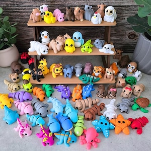 May include: A display of miniature animal figures, including bears, penguins, and sharks, in a variety of colours. The figurines are arranged on a small wooden shelf and a grey surface. The collection features smooth, brightly coloured animal models.