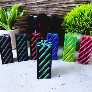 May include: Seven colorful wooden blocks with a diagonal striped pattern. The blocks are arranged in a row on a gray surface. The blocks are green, blue, red, black, green, blue, and red.