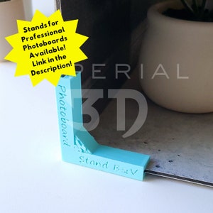 Op de afbeelding: Een lichtblauwe plastic hoekstandaard voor fotoboards. De standaard is gelabeld "Photoboard" en "Stand BV".