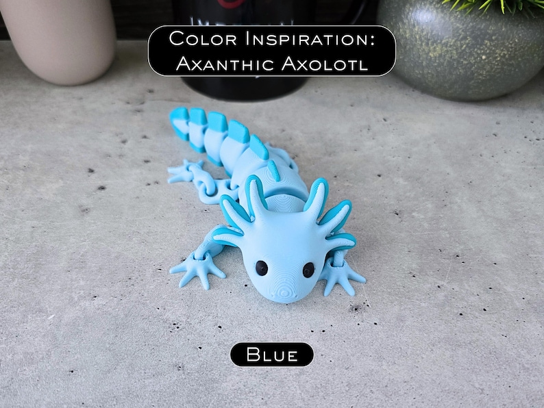 May include: A light blue articulated axolotl figure with dark eyes and a segmented tail. The figure features a light blue body with darker blue accents on the gills and dorsal fin. Text on the image reads: COLOR INSPIRATION: AXANTHIC AXOLOTL and BLUE.