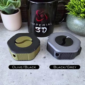 K&ouml;nnte beinhalten: Zwei sechseckige Kabelorganisatoren, einer in Olivgr&uuml;n und Schwarz, der andere in Schwarz und Grau. Beide haben eine schwarze Mitte mit einem Yin-Yang-Symbol. Der Text "Olive/Black" und "Black/Grey" befindet sich unterhalb jedes Organisators.