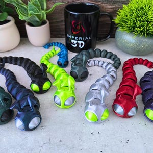May include: Seven colourful segmented worm toys with large eyes. The worms are made of flexible plastic and are available in green, red, silver, black, blue, and dark green.