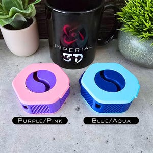 K&ouml;nnte beinhalten: Zwei kleine, sechseckige Beh&auml;lter mit einem Yin-Yang-Symbol-Design. Der Beh&auml;lter links ist rosa mit einem violetten Yin-Yang-Symbol und dem Text "Purple/Pink". Der Beh&auml;lter rechts ist blau mit einem aquafarbenen Yin-Yang-Symbol und dem Text "Blue/Aqua".