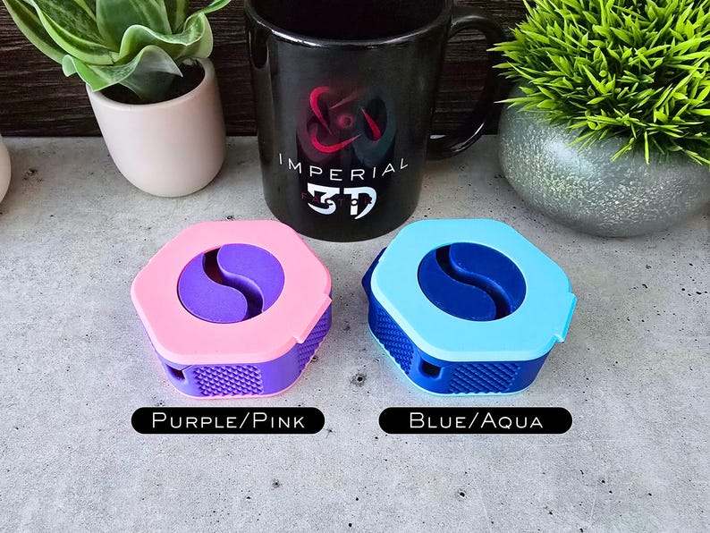 K&ouml;nnte beinhalten: Zwei kleine, sechseckige Beh&auml;lter mit einem Yin-Yang-Symbol-Design. Der Beh&auml;lter links ist rosa mit einem violetten Yin-Yang-Symbol und dem Text "Purple/Pink". Der Beh&auml;lter rechts ist blau mit einem aquafarbenen Yin-Yang-Symbol und dem Text "Blue/Aqua".