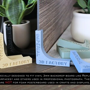 May include: A set of four corner supports for backdrops, made of plastic and printed with the words "Imperial 3D Factory". The supports are in various colors, including blue, green, black, and beige.