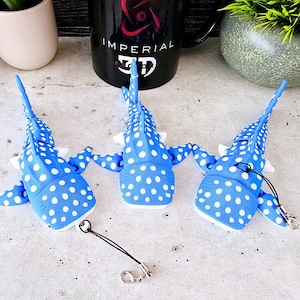 May include: Three blue and white spotted whale shark keychains. The keychains are made of soft, flexible material and have a realistic design.
