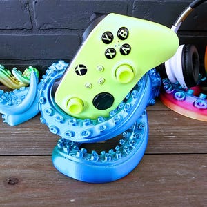 May include: A blue and green 3D printed octopus-shaped stand holds a lime green Xbox controller and a white wireless headset.