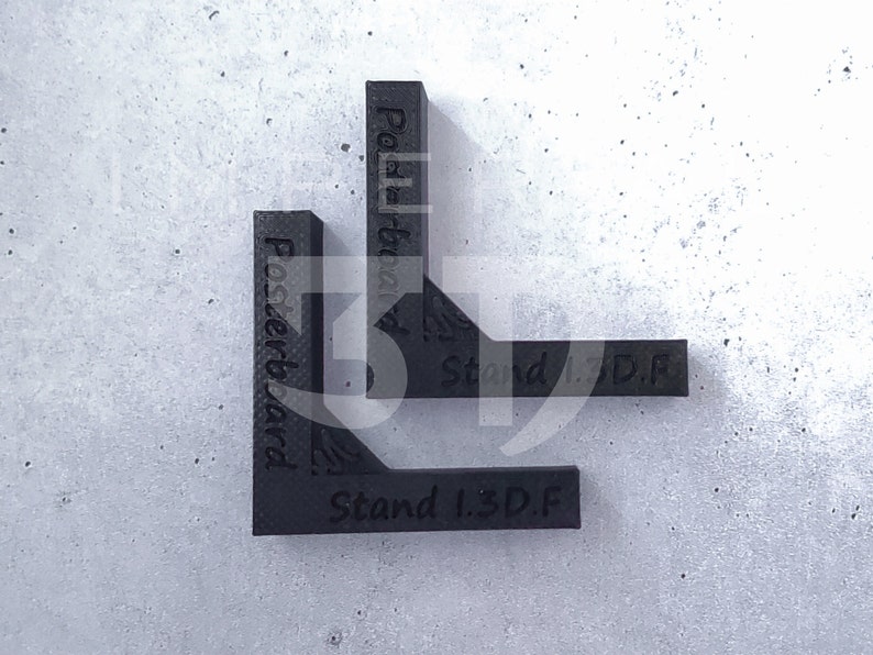 K&ouml;nnte beinhalten: Schwarzes rechtwinkliges Werkzeug mit den W&ouml;rtern "Posterboard" und "Stand 1.3.D.F." aufgedruckt. Das Werkzeug besteht aus einem strukturierten Material und befindet sich auf einer hellgrauen Oberfl&auml;che.