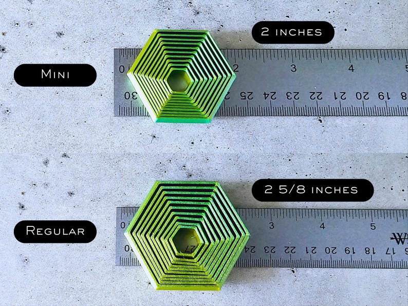 May include: Two green and black hexagonal cookie cutters, one measuring 2 inches and the other measuring 2 5/8 inches. The cookie cutters are made of metal and have a concentric circle design.