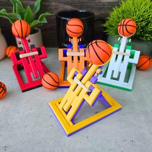 Puede incluir: Una colección de mini aros de baloncesto coloridos con balones de baloncesto adjuntos. Los aros son rojos, naranjas, amarillos y verdes, con detalles morados y blancos. Los balones son naranjas con líneas negras.