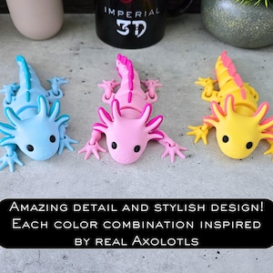 May include: Three articulated axolotl figurines in light blue, pink, and yellow with contrasting dorsal fins and black eyes. The text reads: AMAZING DETAIL AND STYLISH DESIGN! EACH COLOR COMBINATION INSPIRED BY REAL AXOLOTLS.