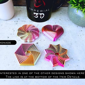May include: Five different cookie cutters in various shapes, including a heart, a star, a flower, and two geometric shapes. The cookie cutters are made of metal and have a pink and orange ombre finish. The text "LEMONADE" is visible at the top of the image.