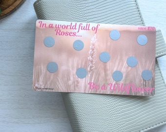 May include: A light gray textured planner with a card that reads "In a world full of Roses... Be a Wildflower." The card has eight gray circles and a wheat stalk design. The card also says "save $70".