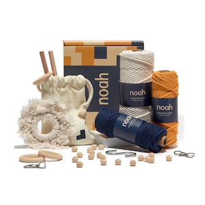 Könnte beinhalten: Ein Makramee-Set mit drei Spulen Baumwollschnur in Natur, Orange und Marineblau, Holzperlen, einem Holzring, einer kleinen Stofftasche und zwei Holzstäben. Das Set ist in einer Schachtel verpackt, auf der das Wort "noah" steht.