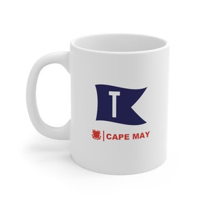 May include: White ceramic mug with a blue and white nautical flag with the letter "T" and the text "CAPE MAY" printed on it.