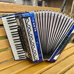 May include: A blue and white accordion with black bellows and a silver trim. The accordion has a white keyboard and a black and white button panel. The accordion is labeled "песня" in white letters.