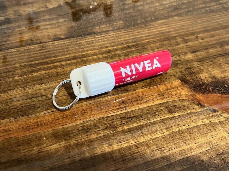 May include: A pink and white NIVEA lip care tube with a silver key ring attached. The tube says "NIVEA CHERRY LIP CARE" on it.