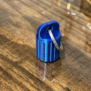 May include: A small, blue, 3D printed keychain with a silver ring. The keychain has a ribbed design.