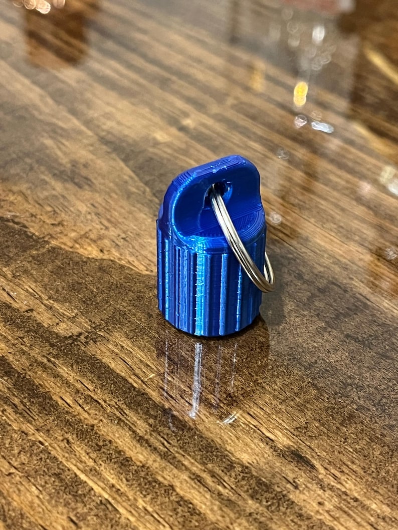 May include: A small, blue, 3D printed keychain with a silver ring. The keychain has a ribbed design.