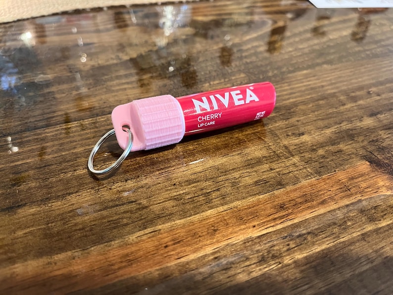 May include: A pink and red NIVEA lip care tube with a silver key chain attached. The tube says "NIVEA CHERRY LIP CARE" on the label.
