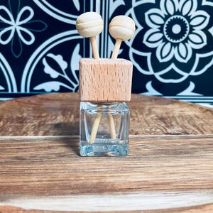 May include: A small glass bottle with a wooden lid and two wooden sticks. The bottle is clear and the lid is a light brown colour. The sticks are inserted into the lid and extend into the bottle.