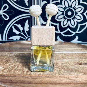 May include: A small glass bottle with a wooden lid and two white diffuser sticks. The bottle is filled with a clear liquid and is sitting on a wooden surface.