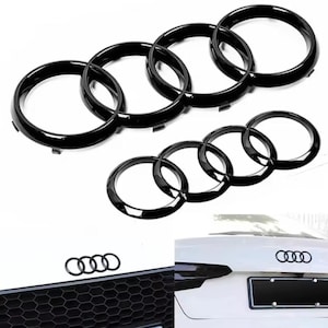 Puede incluir: Anillos negros de emblema de coche, un juego de cinco, se muestran sobre un fondo blanco. Los anillos se muestran en varias disposiciones, incluso en la parrilla delantera y trasera de un coche. El acabado brillante de los anillos es visible.