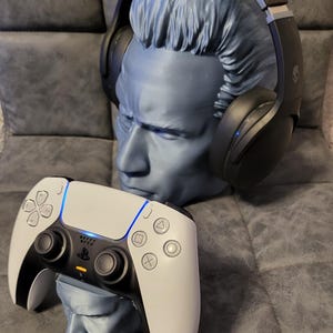 May include: A blue bust supports black headphones. A white and black game controller sits on a smaller bust. The controller has a blue light and the PlayStation logo.