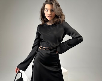 May include: A black satin dress with long sleeves and a lace-up detail at the waist. The dress is fitted and has a mini length.